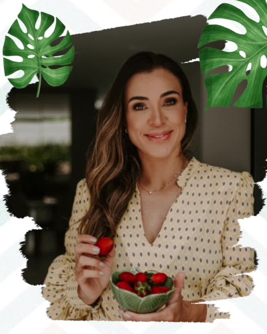 Retrato de Natalie Marques segurando uma tigela de morangos, entre folhas de costela-de-adão.